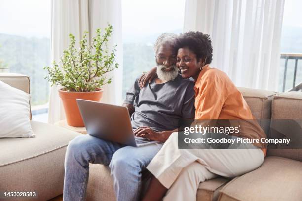 affectionate couple using a laptop in their living room with a scenic view - mature adult couples stock pictures, royalty-free photos & images