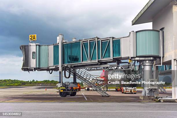 low angle view of a passenger boarding bridge or aerobridge or jet bridge on an overcast day in sibu airport in sarawak, malaysia - passenger boarding bridge stock-fotos und bilder