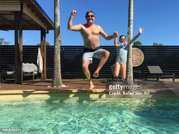 happy father and daughter jumping together into swimming pool on summer holiday - family holidays australia stock pictures, royalty-free photos & images