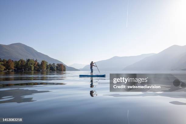 mujer de pie remando en un lago - leisure equipment fotografías e imágenes de stock