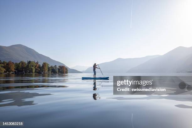 woman stand up paddling on a lake - paddling boat stock pictures, royalty-free photos & images