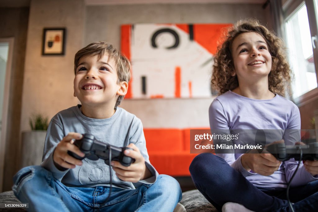Zwei kleine Kinder, Bruder und Schwester spielen Videospielkonsole mit Joystick
