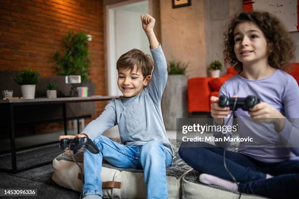deux petits enfants, frère et sœur jouent à la console de jeux vidéo à l’aide d’un joystick - command sisters photos et images de collection