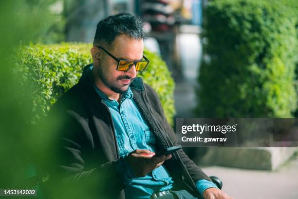 bachelor man uses a smartphone sitting on the park bench. - tinted eyeglasses stock pictures, royalty-free photos & images
