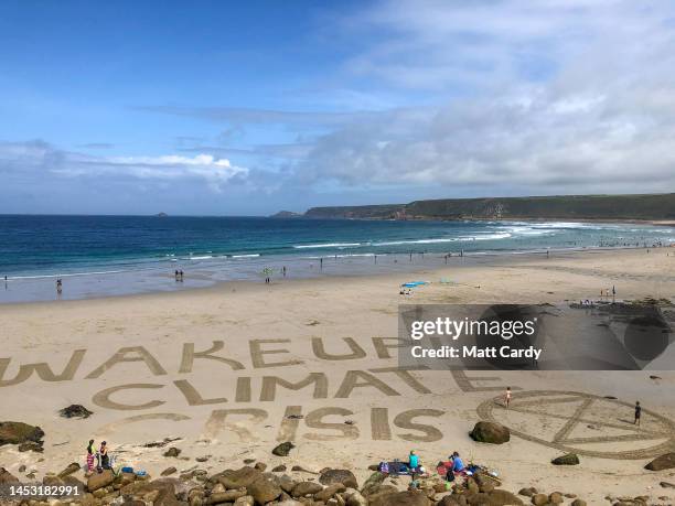 The words Wake Up! Climate Crisis and the Extinction Rebellion sign are drawn in the sand at Sennen Cove on August 15, 2019 in Cornwall, England. The...