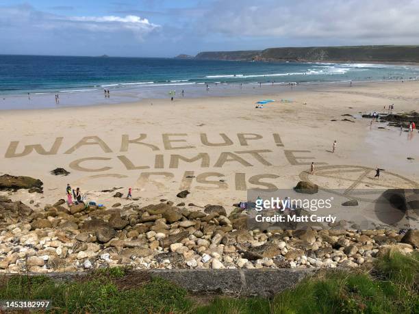 The words Wake Up! Climate Crisis and the Extinction Rebellion sign are drawn in the sand at Sennen Cove on August 15, 2019 in Cornwall, England. The...
