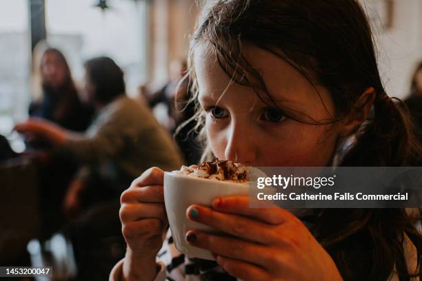 a little girl shelters from the harsh weather, inside a coffee shop. she takes a first sip from her hot cocoa. - adding spice stock pictures, royalty-free photos & images