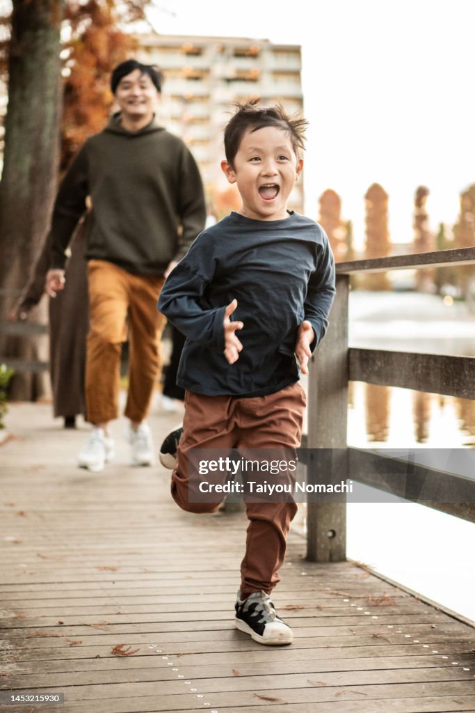 A five-year-old son playing chase with his father in the park.