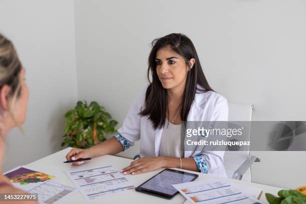 female nutricionist doctor and deportologist in her desk's office during a medical consultation with young woman patient - body mass index chart stock pictures, royalty-free photos & images