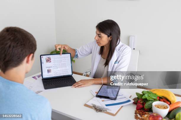 female nutricionist doctor and deportologist in her desk's office during a medical consultation with teenager boy patient - nutritionist stock pictures, royalty-free photos & images