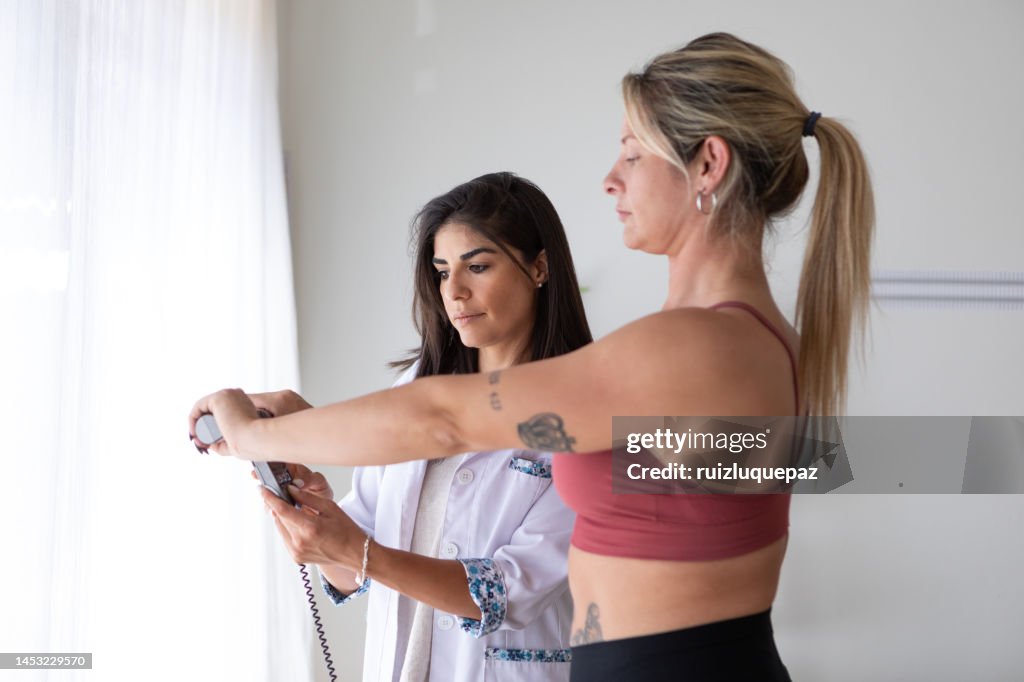 Female nutritionist and deportologist weighing female patient on biometric scale during medical consultation