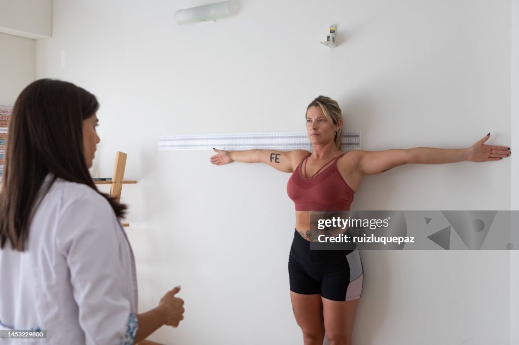 Female nutritionist and deportologist taking arms ans torso limb mesurements of female patient during medical consultation