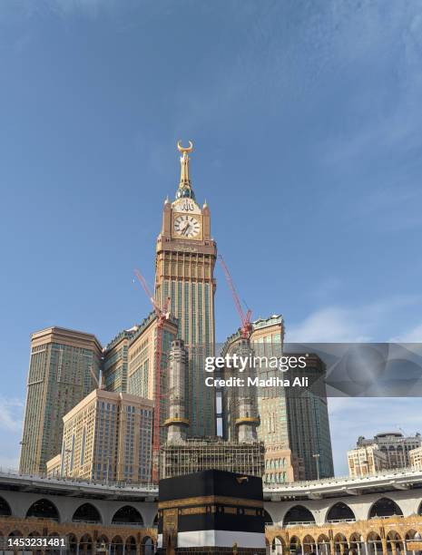clock or mecca / makkah tower near khaana kaaba in holy mosque of al haram while pilgrims doing tawaaf  of kaba for hajj and umrah | motion of people wearing ihram for haj and umra, mecca, saudi arabia |  highest building architecture - kaba at mecca stock pictures, royalty-free photos & images