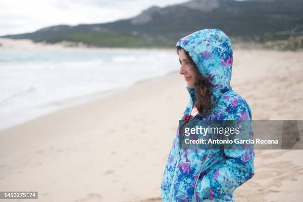 woman in the beach at phone in autumn day looking coast with raincoat - roupa quente imagens e fotografias de stock