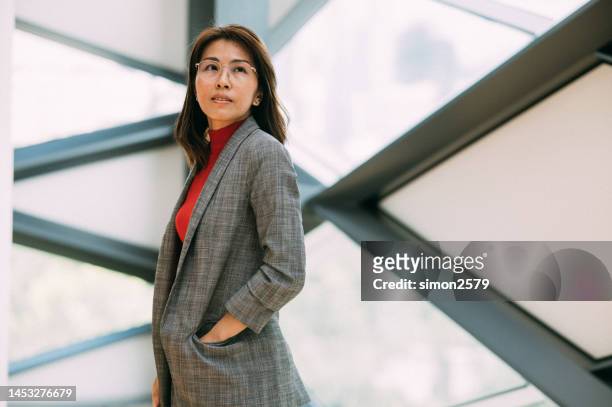 aufnahme einer selbstbewussten asiatischen geschäftsfrau, die in einem modernen büro arbeitet. wegschauende kamera - roter anzug stock-fotos und bilder