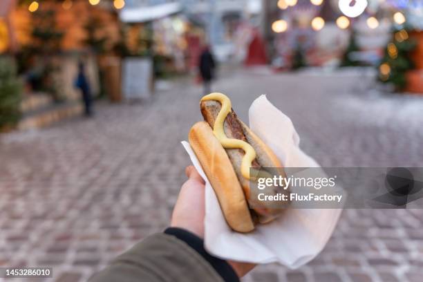 hombre irreconocible sosteniendo bollo con salchicha, en el mercado navideño - salchicha bratwurst fotografías e imágenes de stock