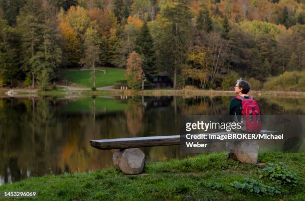 older woman with backpack, best ager, sitting lonely on wooden bench, ebnisee, kaisersbach, autumn, swabian forest, baden-wuerttemberg, germany - best ager woman stockfoto's en -beelden