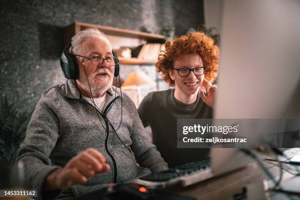 nonno e nipote seduti intorno al tavolo a casa e usando il computer - nonno foto e immagini stock