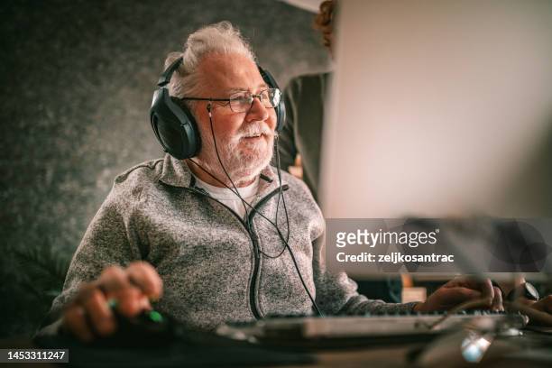 großvater und enkel sitzen zu hause am tisch und benutzen den computer - gaming mobile stock-fotos und bilder
