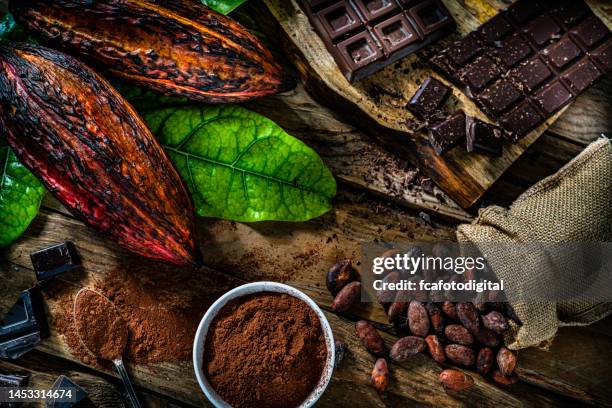 dark chocolate bars, cocoa pods and cocoa powder on rustic wooden table. - cacaopoeder stockfoto's en -beelden