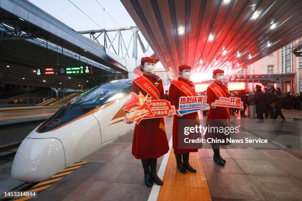 Stewardesses pose for photos next to a Fuxing high-speed train at Beijing Railway Station on December 30, 2022 in Beijing, China. With a length of...