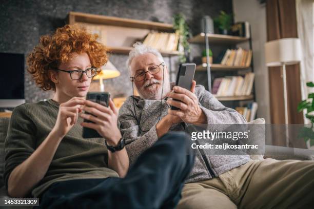 grand-père et petit-fils s’amusent et cherchent un téléphone intelligent - two generation family photos et images de collection