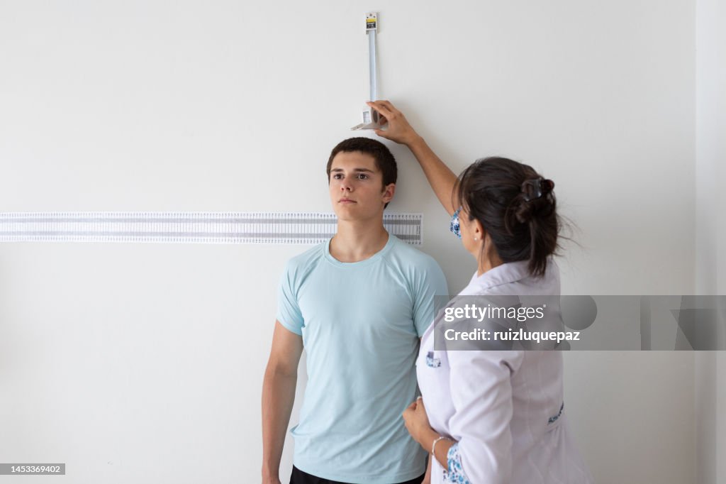 Nutricionista e deportologista do sexo feminino medindo a altura de paciente adolescente durante consulta médica