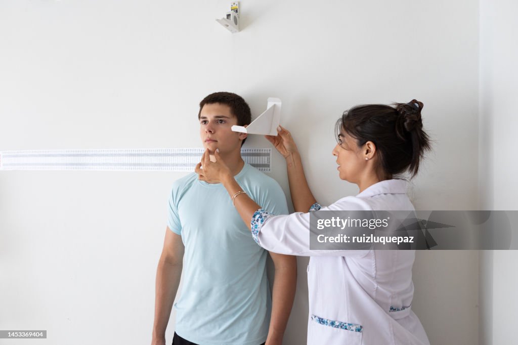 Nutricionista e deportologista do sexo feminino medindo a altura de paciente adolescente durante consulta médica