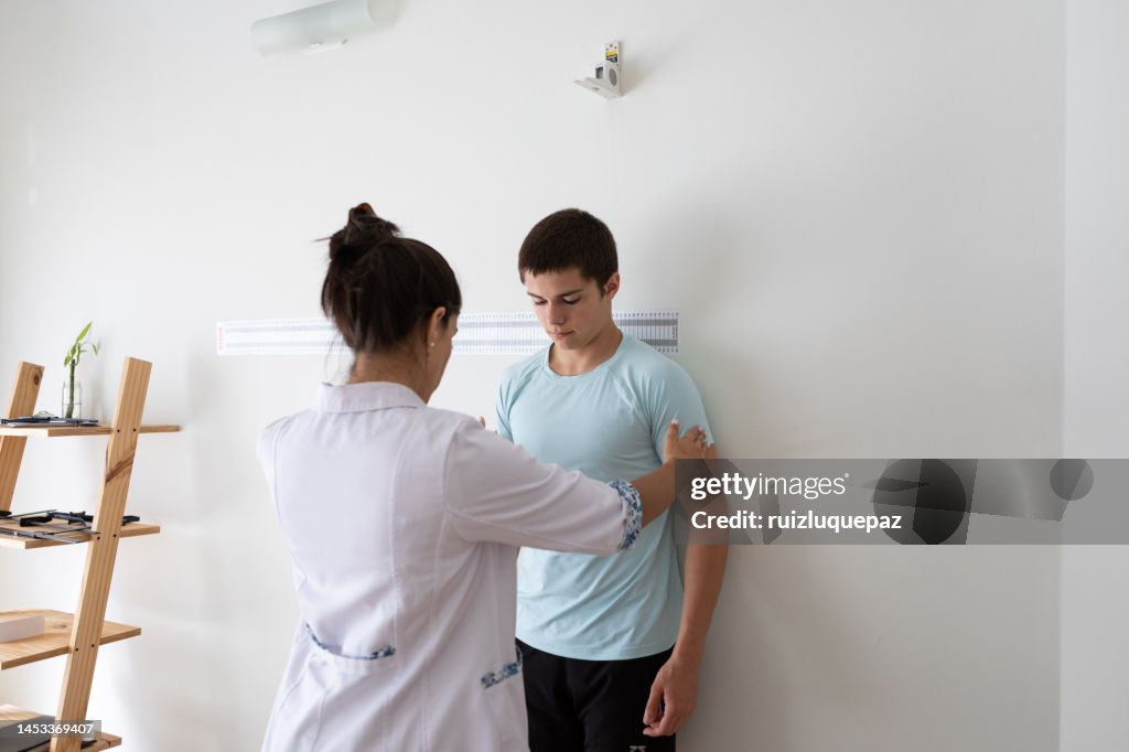 Female nutritionist and deportologist mesuring height of teenager patient during medical consultation