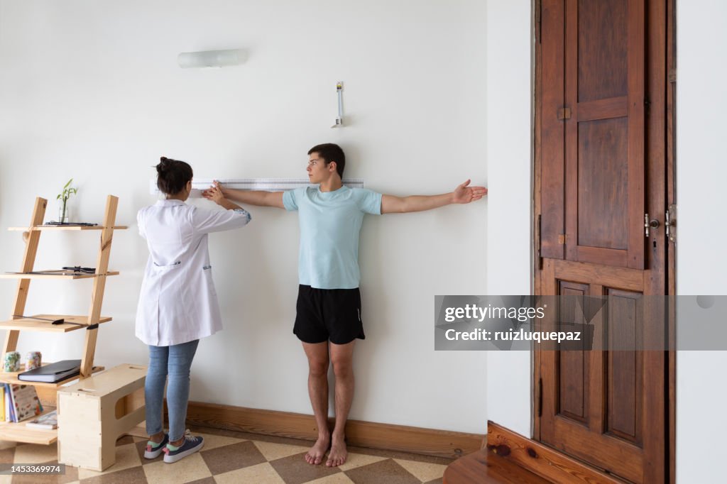 Female nutritionist and deportologist in her office during a medical consultation measuring the arm and torso length of her teenage patient with an anthropometric instrument