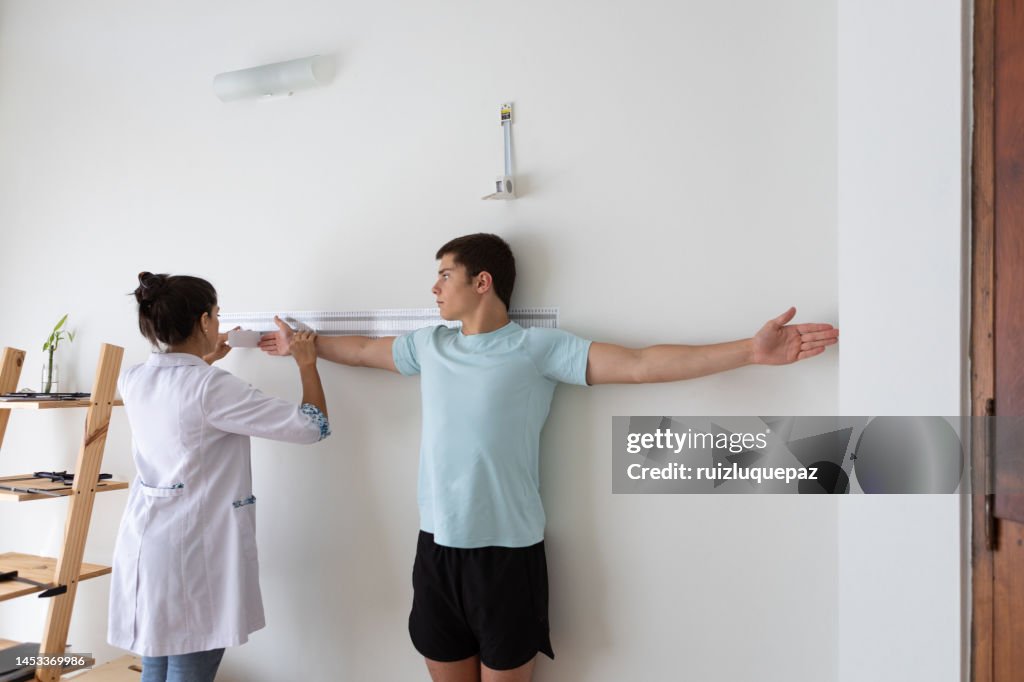 Nutricionista e deportologista em seu consultório durante uma consulta médica medindo o comprimento do braço e do tronco de sua paciente adolescente com um instrumento antropométrico