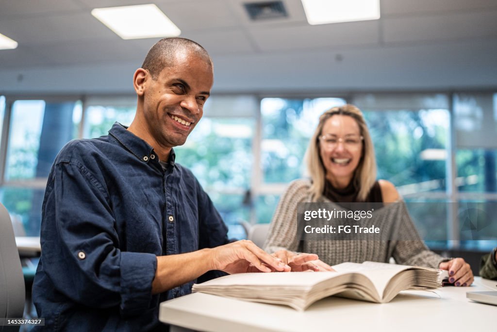 Mid adult man visually impaired man reading a braille book at university