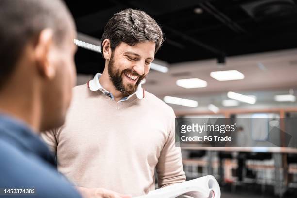 mittlerer erwachsener mann, der sich mit einem freund unterhält, während er an der universität ein buch liest - two men studying library stock-fotos und bilder