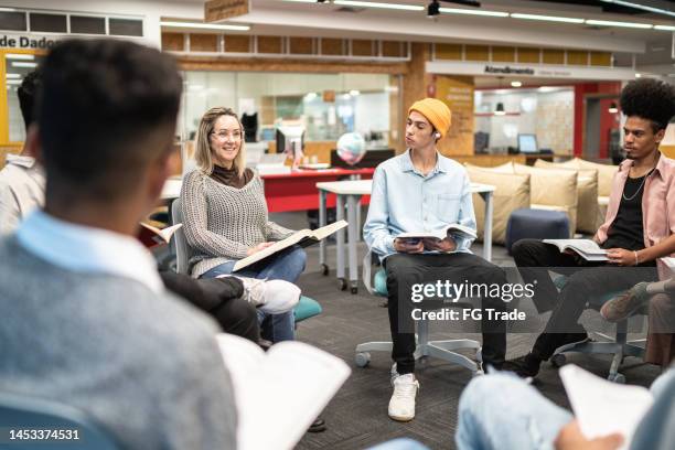 university students reading a book together while talking at university - kunst cultuur en vermaak stockfoto's en -beelden