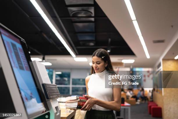 young woman searching for a book in the library system at university - self service stock pictures, royalty-free photos & images