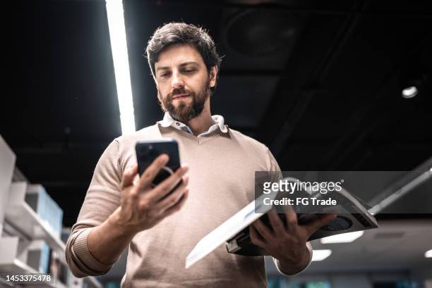 mid adult man using mobile phone while hold a book at university - mobile development stock pictures, royalty-free photos & images
