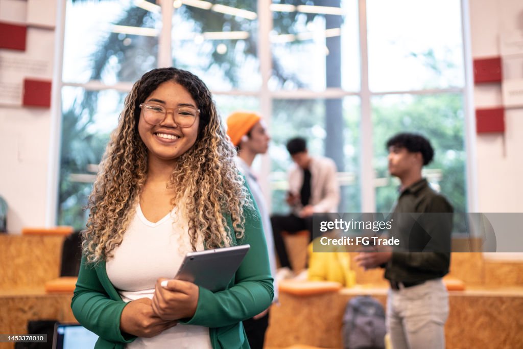 Retrato de uma jovem mulher estudante segurando um tablet digital no auditório da universidade