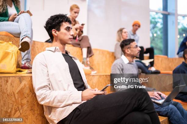 young student man using mobile phone while watch class at university auditorium - community theater stock pictures, royalty-free photos & images