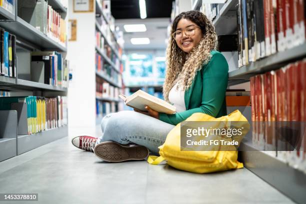 portrait of a young student woman sitting on ground at the university library - brazilian ethnicity stock pictures, royalty-free photos & images