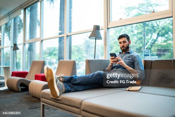 mid adult man using the mobile phone at university - sofa bed stock pictures, royalty-free photos & images