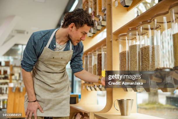 caucasian male employee organizing shelves in a sustainable store - mason jar stock pictures, royalty-free photos & images