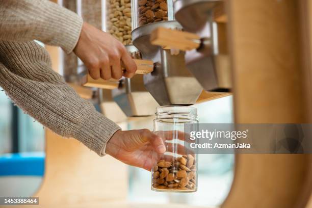 close up of a female using a nuts dispenser in a zero waste store - filling jar stock pictures, royalty-free photos & images