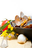 Vertical shot of fresh clams stewed on an iron skillet over white rustic wood table