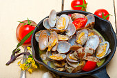 Closeup of fresh clams stewed on an iron skillet over wite rustic wood table