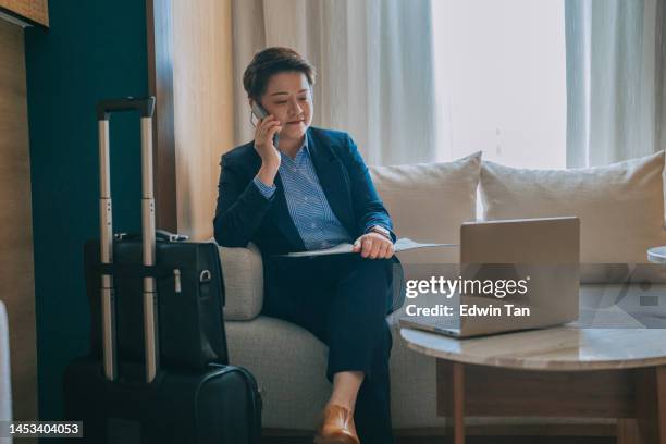 asian chinese businesswoman talking over the phone in hotel room sofa - oxford shoe stock pictures, royalty-free photos & images