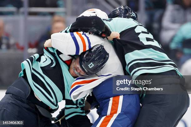 Brandon Tanev is caught in the arms of Klim Kostin of the Edmonton Oilers as Jamie Oleksiak of the Seattle Kraken attempts to separate them during...