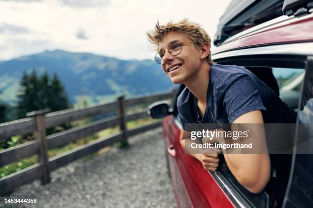 teenage boy looking out of car parked by the road in high austrian alps - boy with car stock pictures, royalty-free photos & images