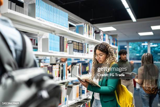 junge studentin liest ein buch in der universitätsbibliothek - buchhandlung stock-fotos und bilder
