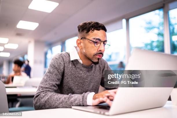 young man working using laptop at coworking or studying at library - library desk stock pictures, royalty-free photos & images
