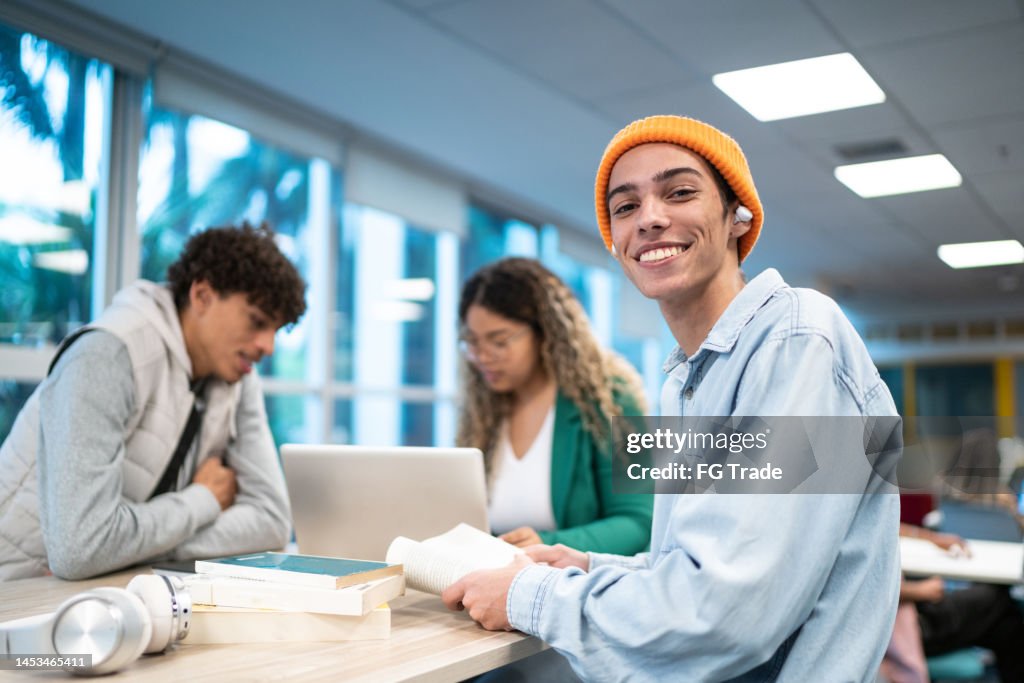 Porträt eines jungen Studenten, während sich seine Freunde im Hintergrund an der Uni/Schule unterhalten